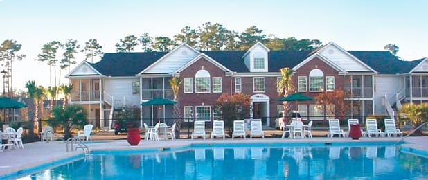 Apartment complex with pool and lounge chairs.
